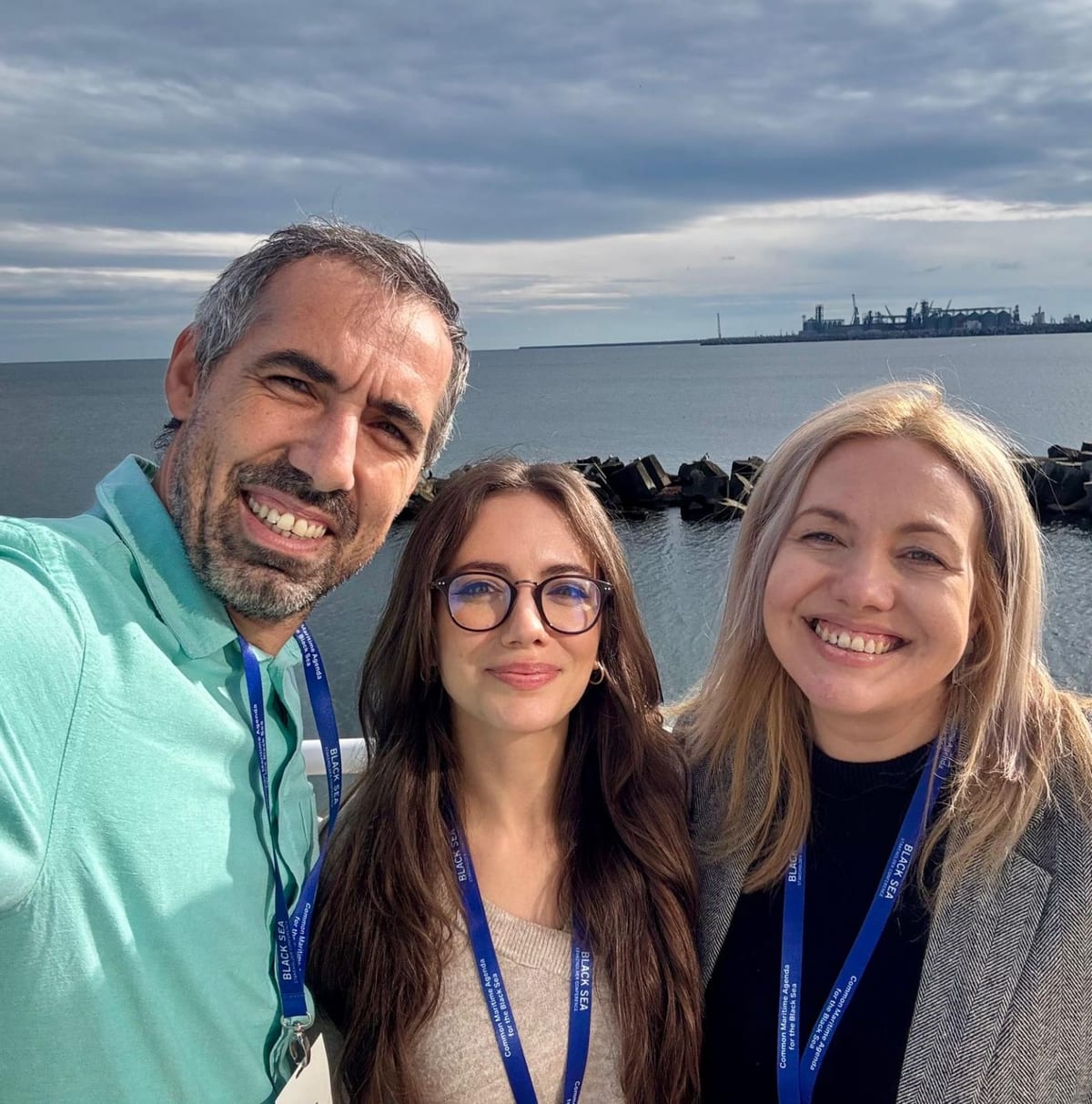 Three Recycllux team members with Black Sea conference lanyards taking a selfie by the sea in Constanța