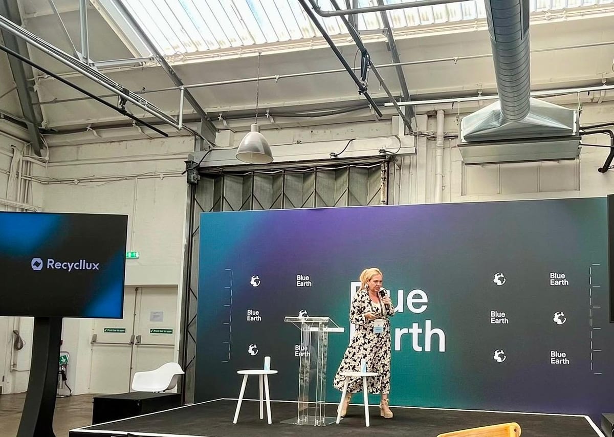 Speaker with a microphone on stage at the Blue Earth Forum in London, with a Recycllux screen to the side